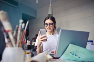 パソコン作業をしながらケータイ画面を見る笑顔の女性